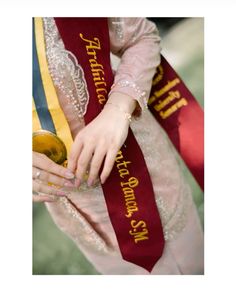 a woman wearing a red and gold sash holding a golden object in her hand with the words,