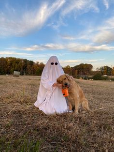 a dog sitting next to a person in a ghost costume and holding an orange object