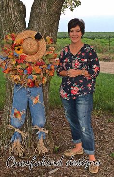 a woman standing next to a tree with a hat on it's head and the words, learn how to make this scarecrow wreath visit oneofhanded designs fb page for details