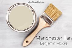 a paint can with a brush next to it on a white wooden background that says manchester tan