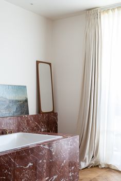 a bath tub sitting next to a window in a room with wooden floors and white walls