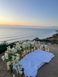 white flowers and candles are arranged on a blanket near the ocean