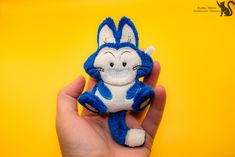 a hand holding a small blue and white cat plush toy on a bright yellow background