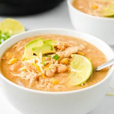 two white bowls filled with soup and garnished with avocado