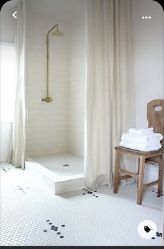 a white bathroom with black and white tile flooring, shower curtain, and wooden chair