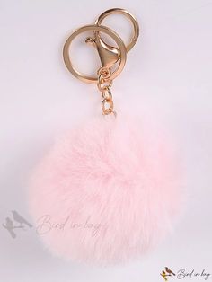 a pink pom - pom keychain hanging from a gold metal hook