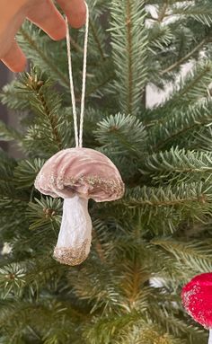 someone is holding a mushroom ornament on a christmas tree