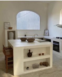 a white kitchen with an island counter and two bowls on the top, in front of a window