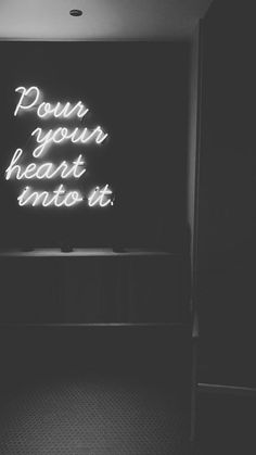 a black and white photo of a neon sign in a dark room with the words pour your heart into it