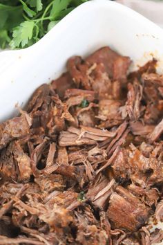 shredded meat in a white casserole dish with parsley