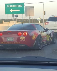 a red sports car is driving down the road in front of a green sign that says turnaround