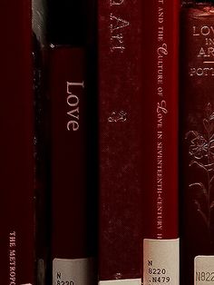 a row of red books sitting on top of a book shelf next to each other