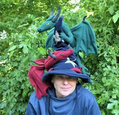 a woman wearing a dragon hat in front of some bushes and trees with her eyes closed