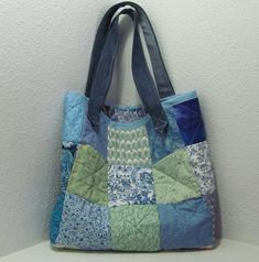 a blue and green patchwork tote bag hanging on a wall next to a white wall