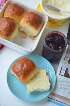 two rolls on a blue plate next to a bowl of jelly and a jar of jam