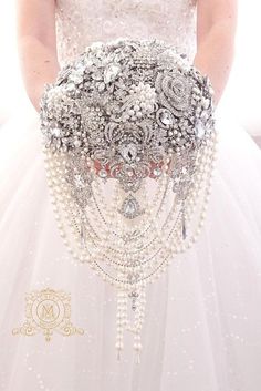 a woman in a wedding dress holding a bridal bouquet with pearls and jewels on it