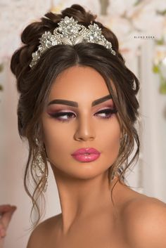 a woman wearing a tiara and makeup looks down at her left shoulder as she poses for the camera