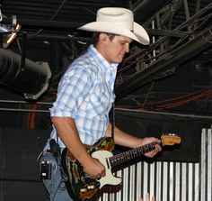 a man in a cowboy hat playing an electric guitar while another person holds his hand out to him