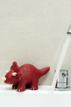 a red toy dinosaur sitting on top of a sink faucet