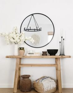 a wooden table with vases and flowers on it in front of a round mirror