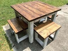 a wooden table and two benches sitting on the sidewalk in front of a grassy area