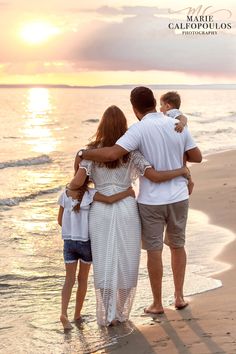 a family standing on the beach at sunset with their arms around each other as they look out into the water