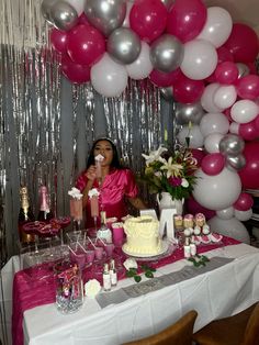 a woman sitting at a table in front of a cake with balloons on the wall