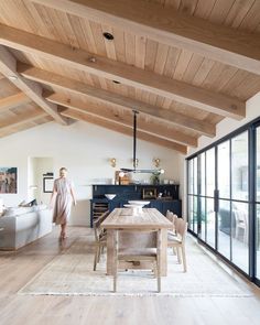 a woman walking through a living room with wooden floors and ceiling beams in the background