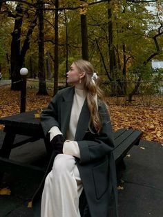 a woman sitting on top of a wooden bench next to a park filled with trees