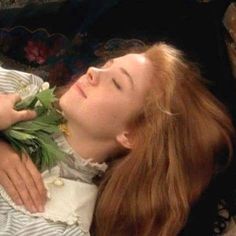 a woman with red hair is laying down and holding flowers in her hands while she sleeps