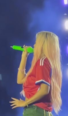 a blonde haired woman with long hair holding a green object in her hand while standing on stage