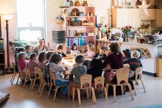 a group of children sitting around a wooden table in a room filled with books and toys