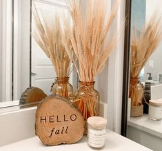 there are two vases with wheat stalks in them on the counter next to a mirror