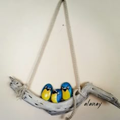 three birds are sitting in a tree branch hanging on the wall, with ropes attached to it