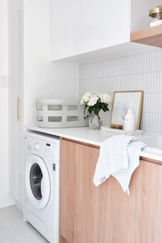 a washer and dryer in a small room with white walls, wood cabinetry, and tile flooring