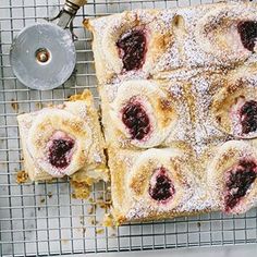 pastries on a cooling rack with powdered sugar and fruit toppings next to a spatula