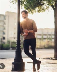 a man standing next to a lamp post on a sidewalk with his hands in his pockets