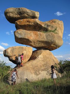 three people standing next to large rocks in the grass