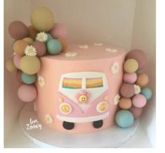 a pink bus cake with flowers and balls around it