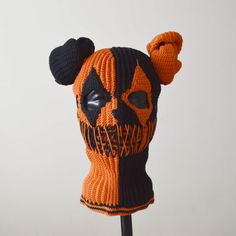 an orange and black knitted skull mask on a stick with a white wall in the background