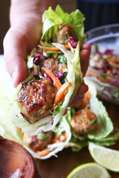 a person holding up a meatball sandwich with lettuce, carrots and slaw