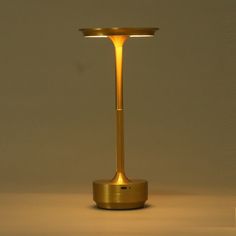 a gold colored table lamp with a dim light on the top and bottom, in front of a white wall