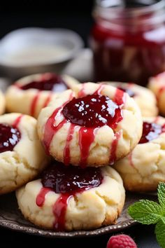 cookies with raspberry sauce and mint leaves on a plate next to jam jars