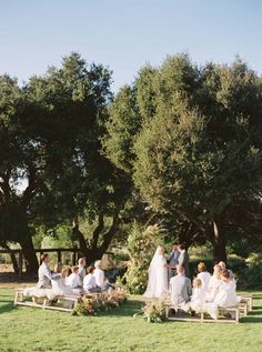 a group of people sitting on top of benches in a field next to some trees