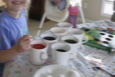 a young boy sitting at a table with cups and saucers on it, smiling for the camera