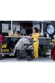 a woman standing next to a baby stroller in front of a food cart with flowers on it