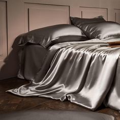 a bed with silver sheets and pillows on top of it in a room that has wooden floors