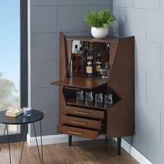 a cabinet with liquor bottles and glasses in it next to a table that has a potted plant on top