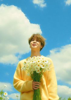 a woman holding flowers in her hands and looking up into the sky with clouds behind her