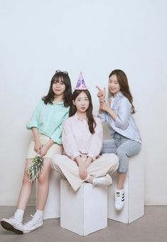 three young women sitting on top of each other posing for a photo with a birthday hat